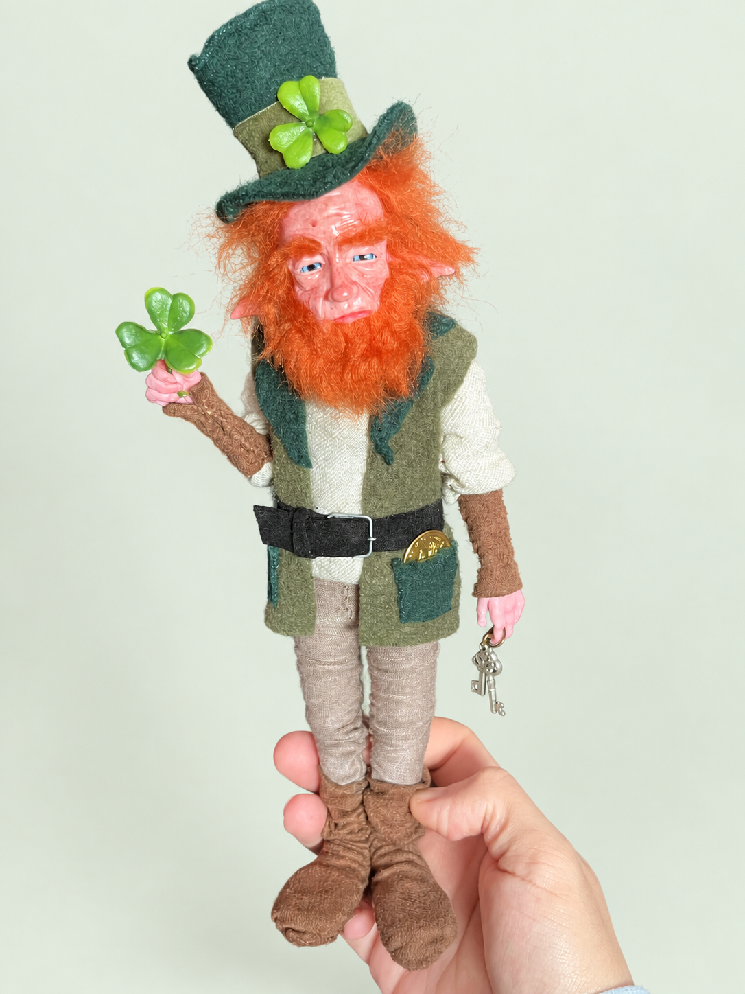 Lenny Leprechaun — en mano, referencia de tamaño — fondo salvia suave claro