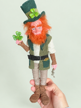 Lenny Leprechaun — en mano, referencia de tamaño — fondo salvia suave claro